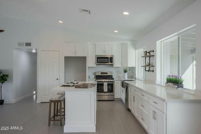 kitchen with stainless steel appliances, visible vents, white cabinetry, vaulted ceiling, and a kitchen bar