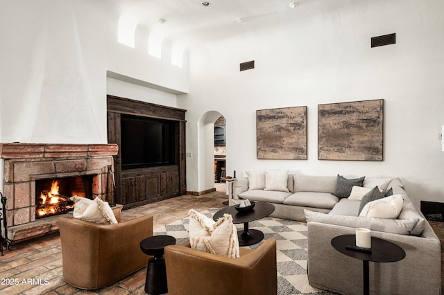 living room featuring visible vents, arched walkways, a fireplace, and a towering ceiling