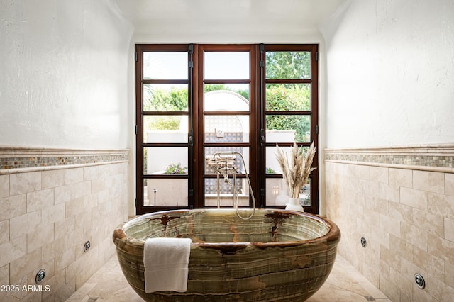 interior space with tile walls, a wainscoted wall, and a soaking tub