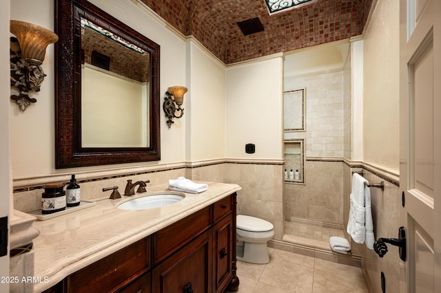 full bathroom featuring a tile shower, tile walls, a wainscoted wall, toilet, and vanity