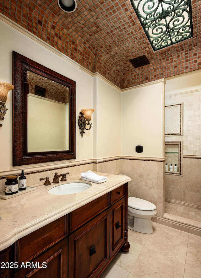 bathroom with a tile shower, tile walls, toilet, brick ceiling, and vanity