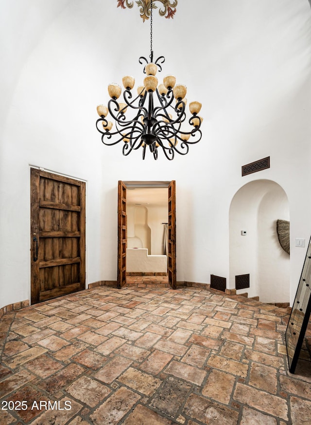 foyer entrance with a chandelier, visible vents, baseboards, a towering ceiling, and arched walkways