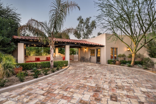 exterior space featuring stucco siding, exterior kitchen, a tiled roof, and a patio area