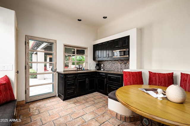 kitchen featuring stainless steel microwave, a sink, dark cabinetry, and decorative backsplash