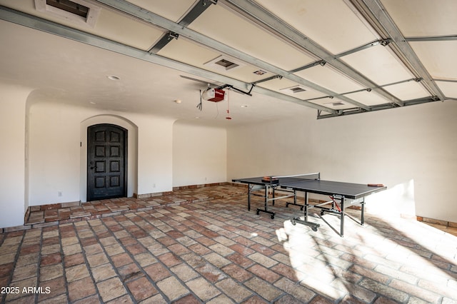 recreation room featuring a garage, baseboards, brick floor, and arched walkways