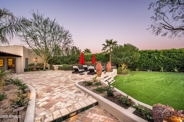 patio terrace at dusk featuring a yard