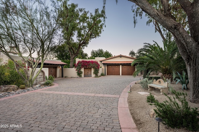 mediterranean / spanish house with a garage, stucco siding, a tile roof, and decorative driveway