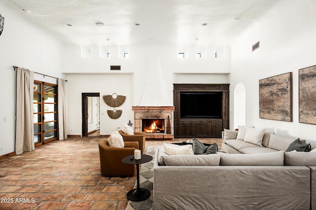 living area with a towering ceiling, visible vents, baseboards, and a warm lit fireplace