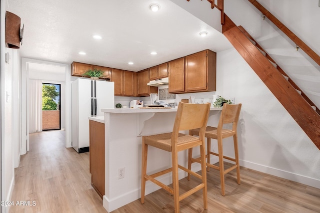 kitchen with a breakfast bar, brown cabinets, light countertops, freestanding refrigerator, and under cabinet range hood