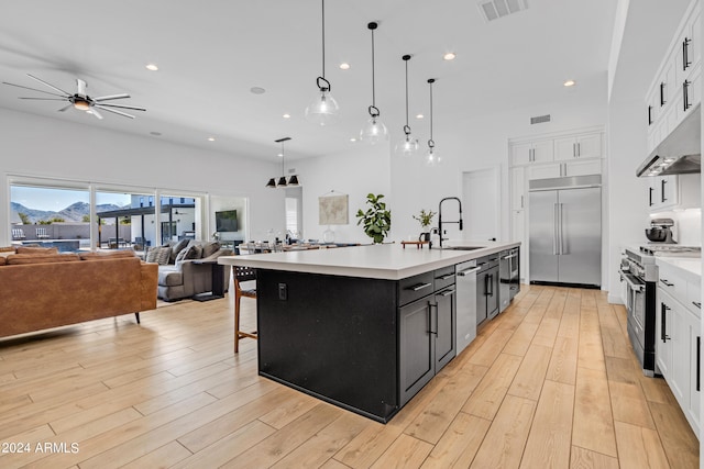 kitchen featuring light wood-type flooring, a kitchen island with sink, high end appliances, decorative light fixtures, and ceiling fan