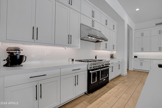 kitchen featuring white cabinets, backsplash, light stone countertops, light wood-type flooring, and double oven range