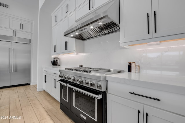 kitchen featuring premium appliances, light wood-type flooring, white cabinetry, and light stone counters