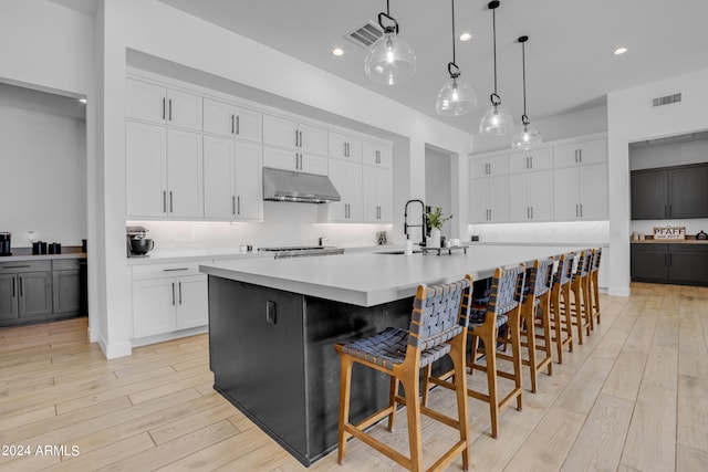 kitchen with hanging light fixtures, white cabinetry, light hardwood / wood-style flooring, a large island, and sink