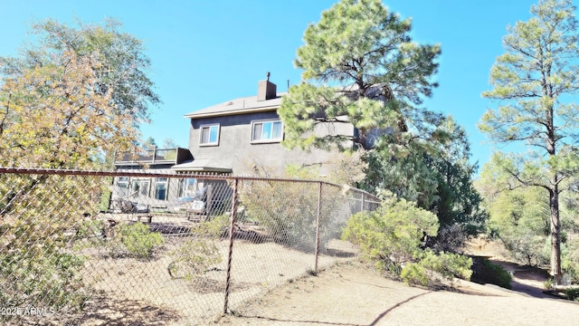 back of property featuring fence, a chimney, and stucco siding