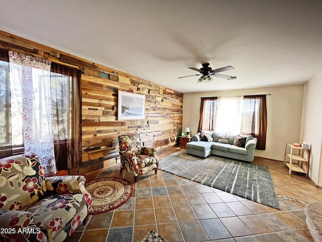 living area featuring a ceiling fan, visible vents, and wooden walls