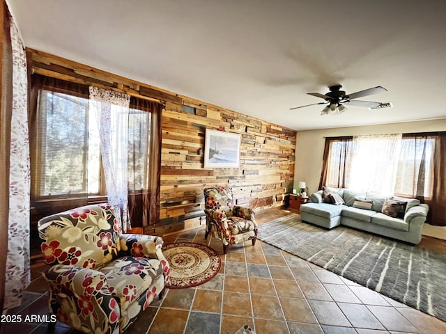 living room featuring wood walls, visible vents, and a ceiling fan