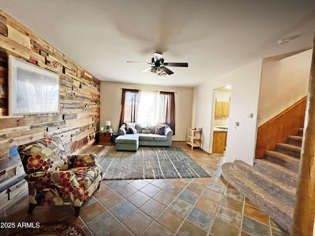 living area featuring ceiling fan, wood walls, and stairs