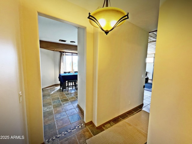 hall featuring stone tile flooring, visible vents, and baseboards