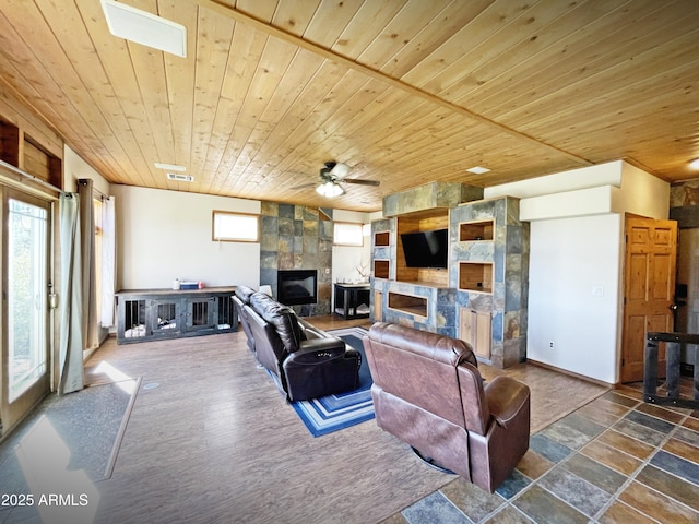 living room featuring a fireplace, visible vents, stone finish floor, wood ceiling, and ceiling fan