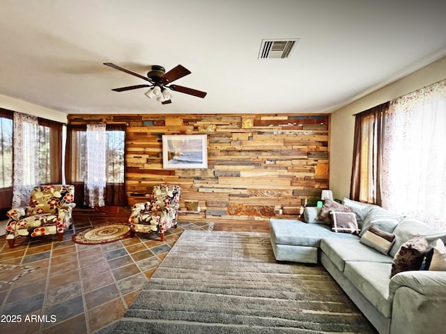 living room with ceiling fan, wooden walls, visible vents, and a wealth of natural light