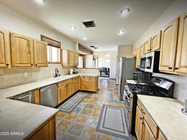 kitchen with visible vents, decorative backsplash, a peninsula, stainless steel appliances, and a sink