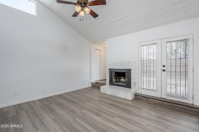 unfurnished living room featuring lofted ceiling, a ceiling fan, wood finished floors, a high end fireplace, and healthy amount of natural light