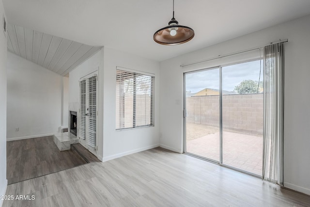 unfurnished living room featuring plenty of natural light, wood finished floors, and a fireplace with raised hearth