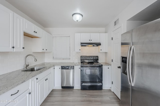 kitchen with appliances with stainless steel finishes, under cabinet range hood, a sink, light wood finished floors, and white cabinets