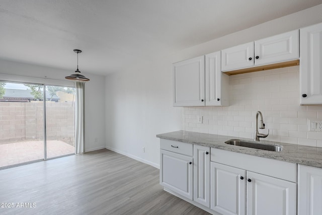 kitchen with a sink, backsplash, white cabinetry, baseboards, and light wood-type flooring