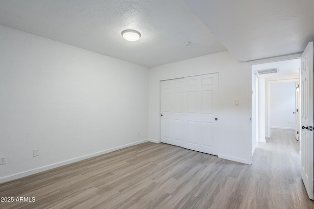 unfurnished bedroom featuring light wood-style floors, baseboards, a closet, and a textured ceiling