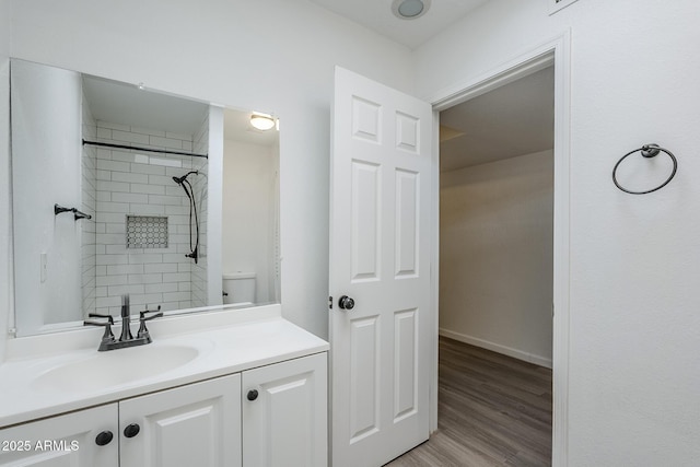 full bathroom with vanity, a tile shower, wood finished floors, baseboards, and toilet