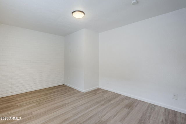 spare room with wood finished floors, baseboards, brick wall, and a smoke detector