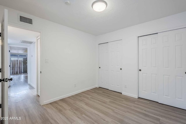 unfurnished bedroom featuring two closets, light wood-style floors, and baseboards
