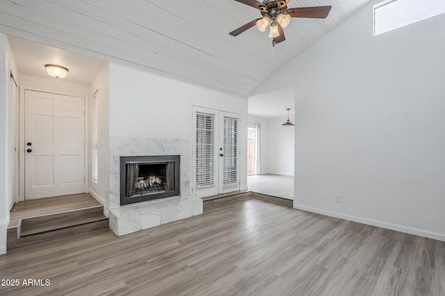 unfurnished living room with wood finished floors, a ceiling fan, a high end fireplace, high vaulted ceiling, and baseboards