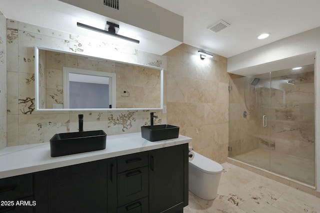 bathroom with toilet, double vanity, a sink, and tile walls