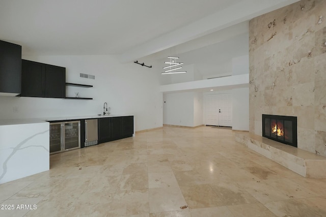 unfurnished living room with high vaulted ceiling, a sink, visible vents, beam ceiling, and a tiled fireplace