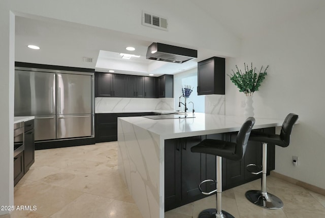 kitchen featuring a peninsula, built in refrigerator, a kitchen bar, and light countertops