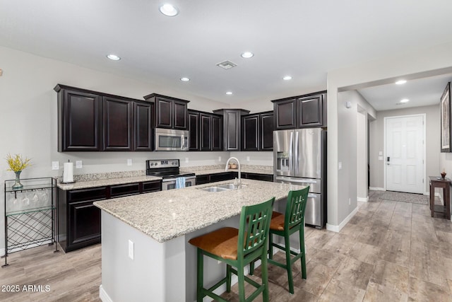 kitchen with a center island with sink, appliances with stainless steel finishes, a breakfast bar area, light stone countertops, and a sink