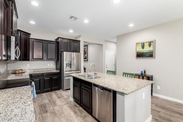 kitchen with a sink, visible vents, appliances with stainless steel finishes, light stone countertops, and a center island with sink