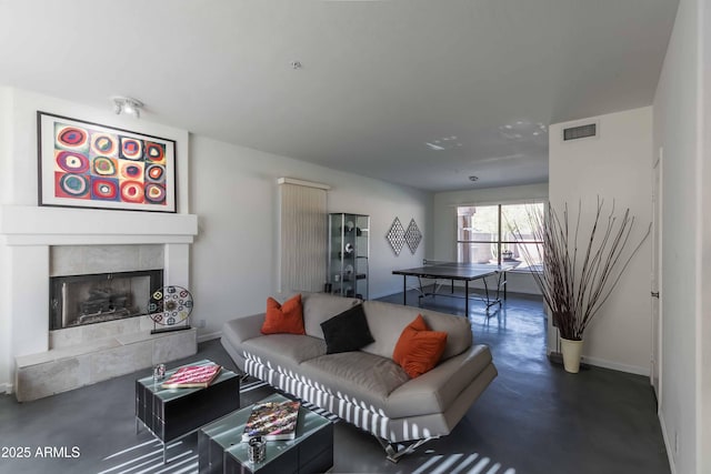 living area with finished concrete flooring, a tile fireplace, visible vents, and baseboards