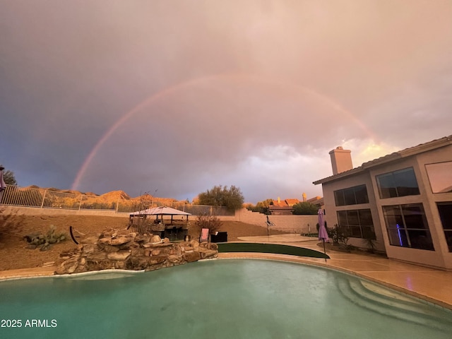 pool at dusk featuring a patio, fence, and an outdoor pool