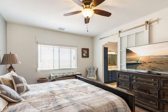 bedroom with ceiling fan, a barn door, and ensuite bath