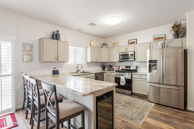 kitchen with sink, beverage cooler, stainless steel appliances, dark hardwood / wood-style flooring, and kitchen peninsula