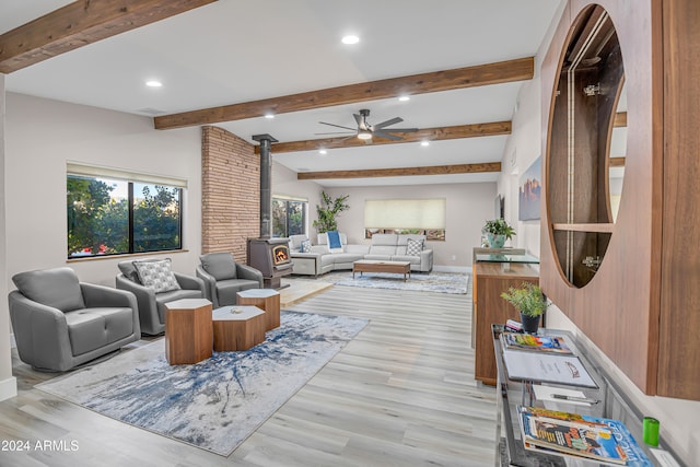 living room featuring lofted ceiling with beams, a wood stove, light hardwood / wood-style floors, and ceiling fan