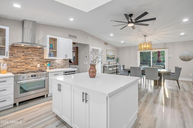 kitchen with wall chimney exhaust hood, a kitchen island, white cabinets, and stainless steel range