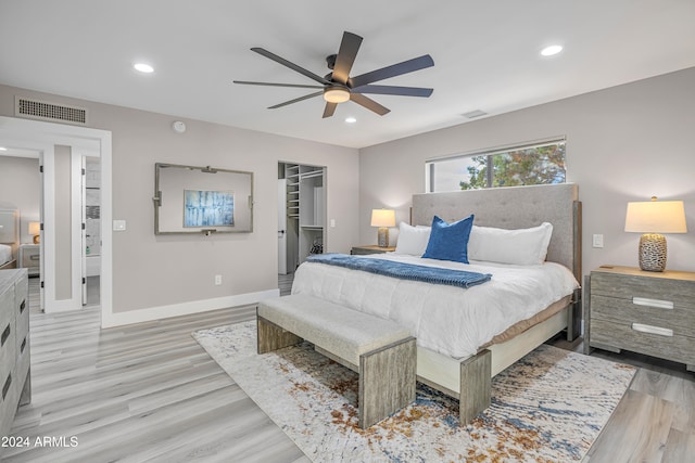 bedroom featuring ceiling fan, light hardwood / wood-style flooring, a closet, and a walk in closet