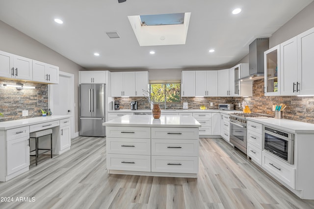 kitchen with wall chimney exhaust hood, white cabinets, a skylight, and premium appliances