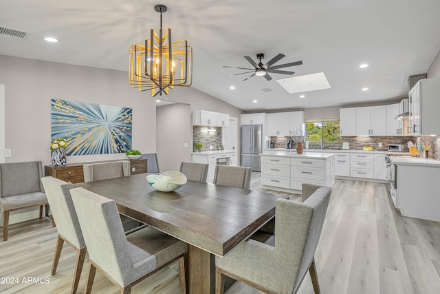 dining area featuring vaulted ceiling with skylight, ceiling fan with notable chandelier, and light wood-type flooring