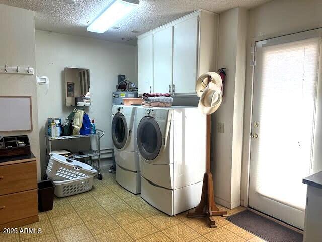 clothes washing area featuring a textured ceiling, a wealth of natural light, cabinets, and washing machine and clothes dryer