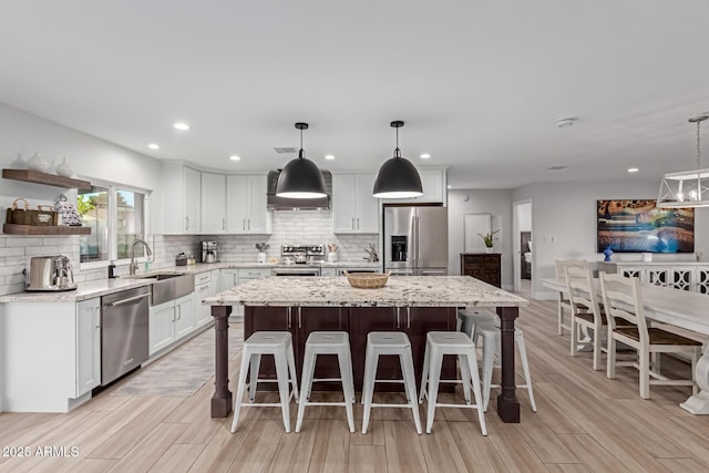 kitchen featuring sink, hanging light fixtures, appliances with stainless steel finishes, a kitchen island, and light stone countertops